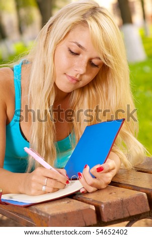 Girl-student in park writes in writing-book.