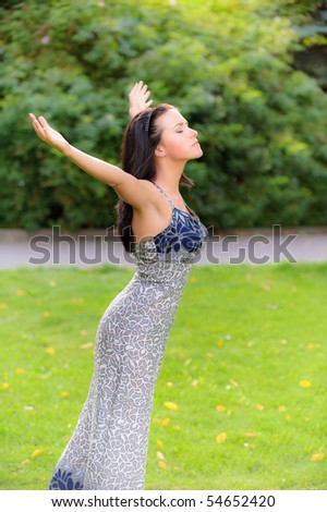 Dark-haired charming girl stands on lawn and enthusiastically lifts upwards hands.