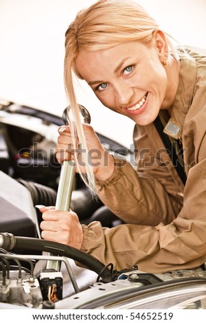 Woman car mechanician repairs engine of car and smiles.