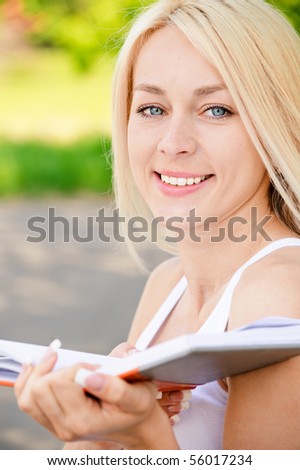 Smiling girl-student reads textbook against summer nature.