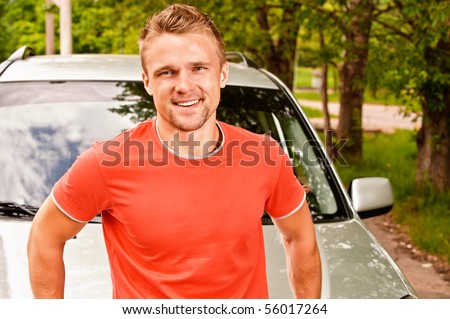 Driver of car stands about cowl and smiles against summer nature.