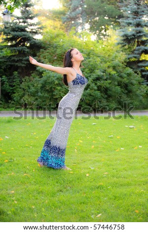 Dark-haired charming girl stands on lawn and enthusiastically lifts upwards hands.