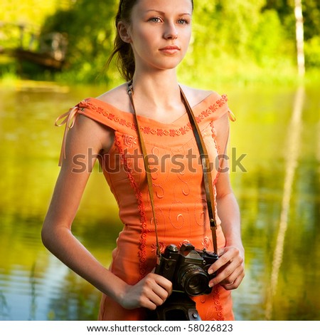 Charming girl with camera stands on bank of beautiful lake.