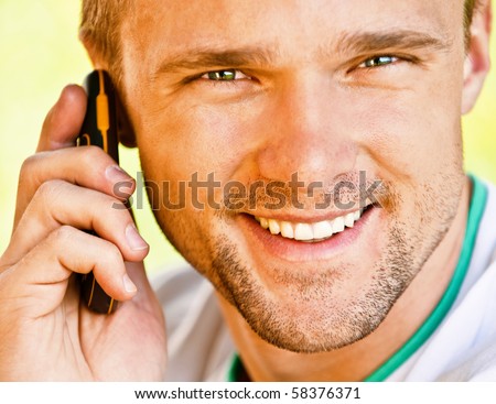 Young man smiles and speaks on phone, close up.