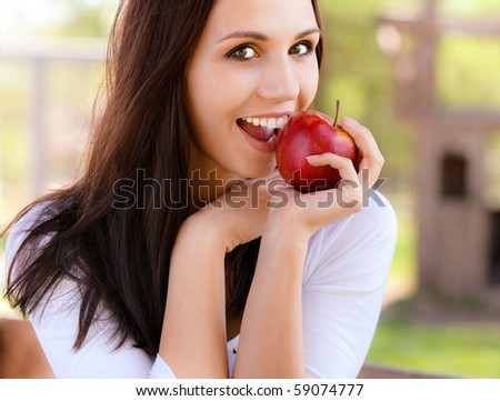 Smiling young woman bites red apple