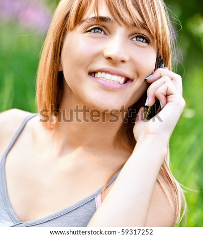 Beautiful smiling girl speaks by mobile phone against summer green nature.