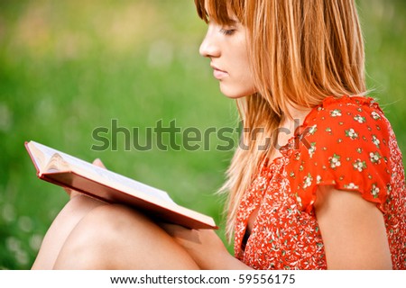 Beautiful young woman reads book, on green summer background.