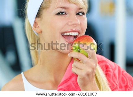 portrait of happy sporty blonde girl eating apple in gym