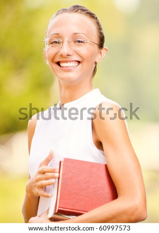 Portrait of beautiful laughing girl-student with book against summer green park.