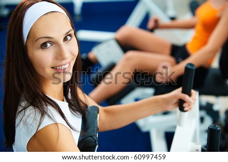 portrait of girl exercising in gym. other girl on multi gym out of focus on background.