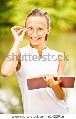 Girl-student in glasses smiles and reads book, against summer green park.