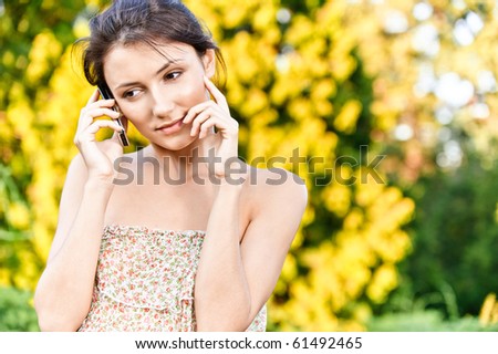 Young beautiful woman talks by mobile phone, against autumn nature.