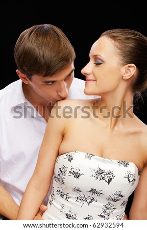 portrait of young romantic couple on black. man kissing woman\'s shoulder and she is closing her eyes