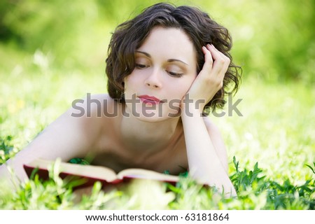 outside portrait of beautiful curly girl laying on grass and reading book in park