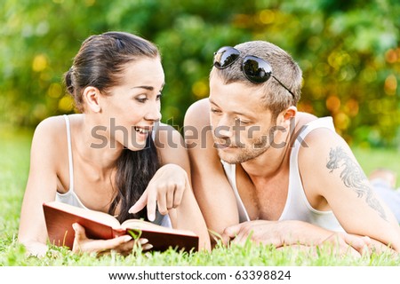 Beautiful couple lies on grass and reads book.