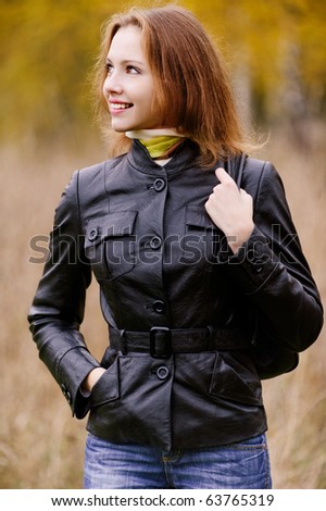 Young beautiful smiling woman with ladies\' handbag looks in profile against autumn park.