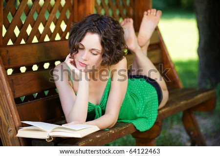 outside portrait of young beautiful curly woman laying on bench and reading book in park