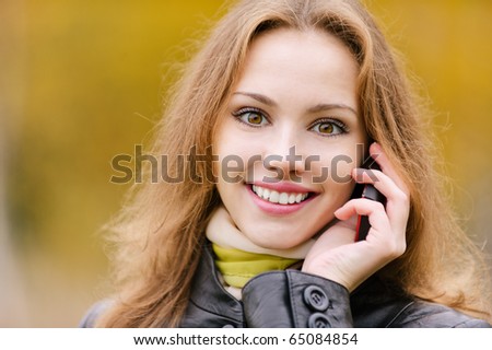 Young beautiful woman smiles and talks on cellular telephone, close up, against yellow autumn nature.