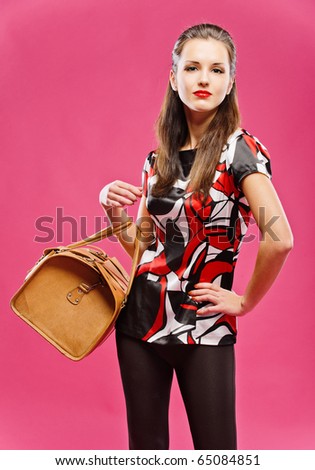 Young beautiful dark-haired girl has control over leather brown bag, on red background.