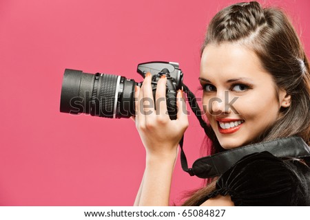 Young beautiful smiling woman-photographer hold in hands DSLR, going to make picture, on red background.