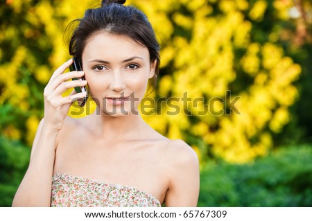 Young beautiful woman talks by mobile phone, against autumn nature.