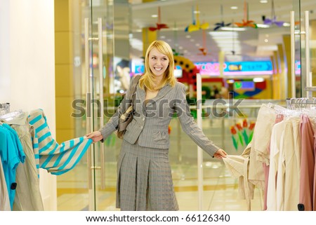 The beautiful young woman laughs in a lady's wear shop - she cannot choose the best blouse.