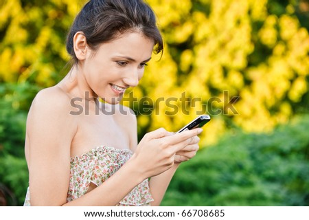 Young beautiful woman read sms by mobile phone, against autumn nature.