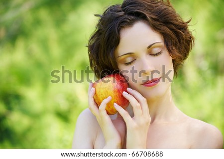 outside portrait of beautiful young curly woman with eyes shut with red apple in park