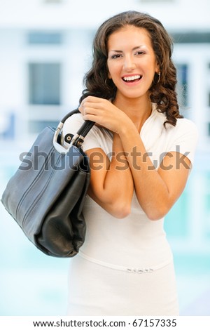Young beautiful brunette with flowing hair in white clothes has control over ladies\' handbag and laughs.