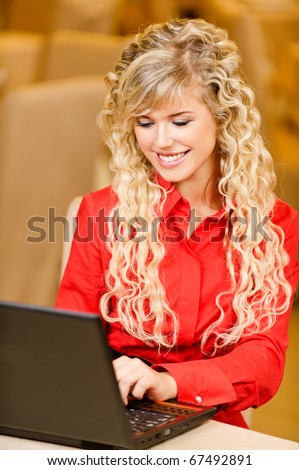 Young charming smiling woman-student works on black laptop against beautiful interior.
