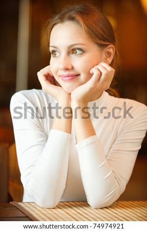 Young beautiful woman sits in cozy cafe and looks out of window