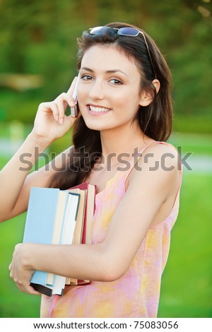 pretty girl-student holds a book and talking on a cell phone on the natural background