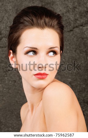 Portrait of charming dark-haired girl with bared shoulders, against a dark background.