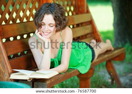 outside portrait of young beautiful happy woman laying on bench and reading book in park