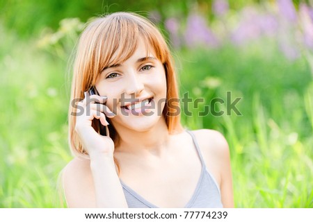 Beautiful smiling girl speaks by mobile phone against summer green nature.