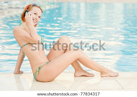 Young beautiful smiling woman in bikini in warm pool on resort and talk in mobile phone.