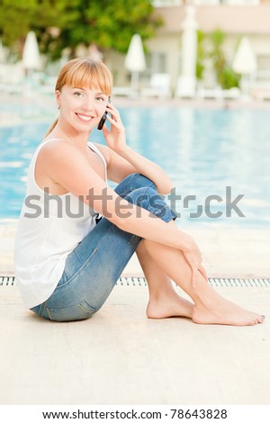 Young beautiful smiling woman in jeans nearby warm pool on resort speak on mobile phone.