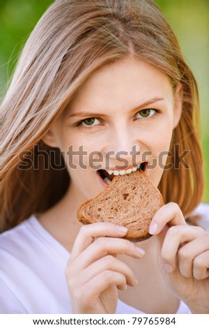 Young beautiful woman bites piece of stale bread, on green background of summer city park.