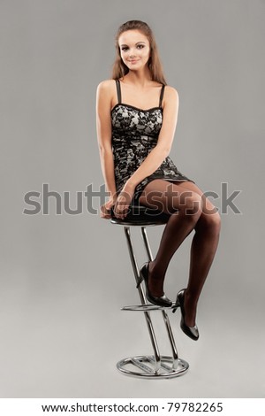 Young beautiful woman sits on bar chair and smiles, on gray background.