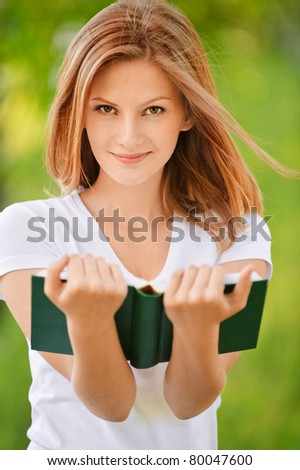 Portrait of nice young smiling woman with book on green background of city park.