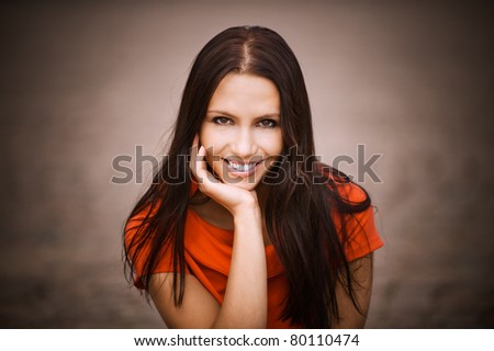 Beautiful young woman in red dress props up hand chin and laughs.