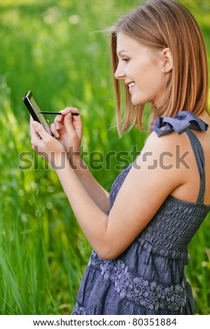 Young attractive woman writes in communicator with help stylus, on green background of summer city park.