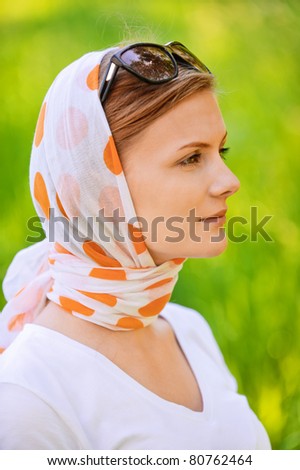 portrait of young beautiful woman wearing shawl, white blouse and sunglasses, standing at summer green park