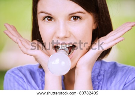 Close-up portrait of young funny amazed woman holding light bulb in teeth.