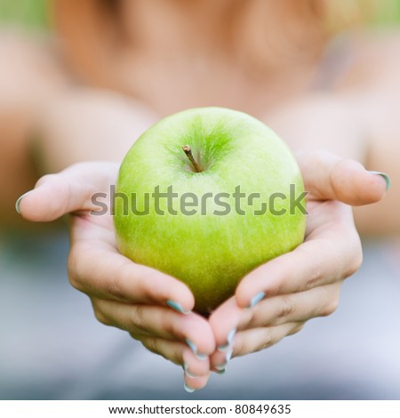 Woman with green big apple, against green summer garden.