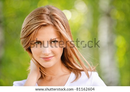 close-up portrait of beautiful young blond woman in white blouse at park holding her neck
