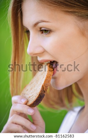 portrait of young beautiful woman eating bread in summer green park