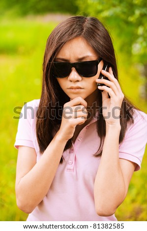 Portrait of mysterious beautiful woman in sunglasses speaking on telephone in summer green park.
