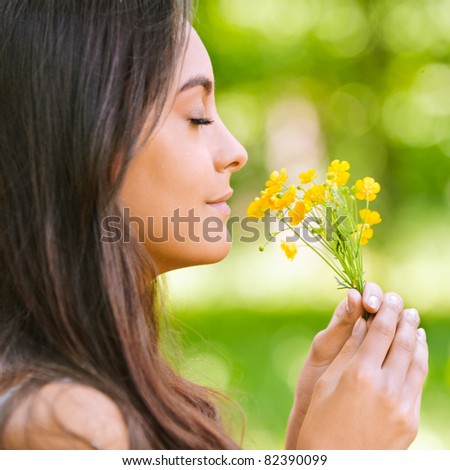 Young beautiful smiling woman smells small bouquet of yellow florets, against green summer garden.
