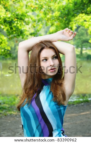 Portrait of young beautiful brunette woman wearing blue blouse and holding arms up at summer green park.